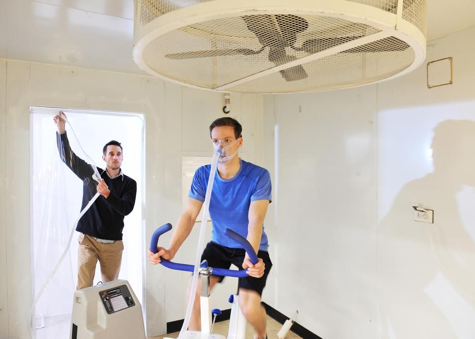 <p>Cette chambre hypoxique, qui vient d'être construite au Département de kinésiologie, permet de recréer l'atmosphère pauvre en oxygène qu'on trouve en altitude. Elle sera utilisée par François Billaut, en arrière-plan, pour ses projets de recherche portant sur les effets physiologiques de l'exposition à l'hypoxie. Des athlètes d'élite de la région de Québec y auront aussi recours pour leur entraînement. Mathieu Lanoue, un membre de l'équipe du professeur Billaut, démontre l'un des usages possibles de cet équipement.</p>