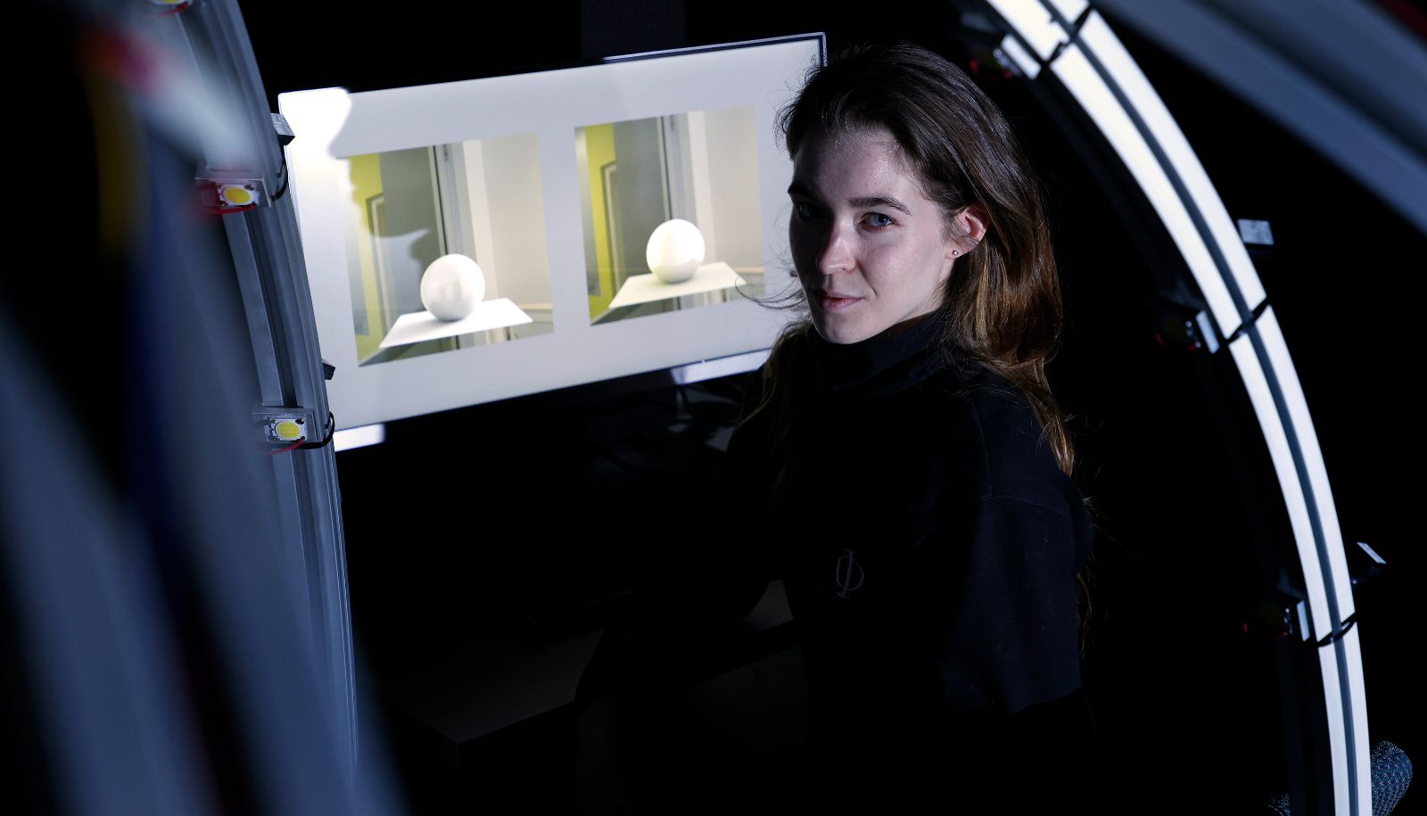 <p>La doctorante Justine Giroux dans la pièce sombre qui était utilisée pour les tests, avec deux exemples d'éclairage à l'écran parmi lesquels les participantes et participants devaient choisir. </p>