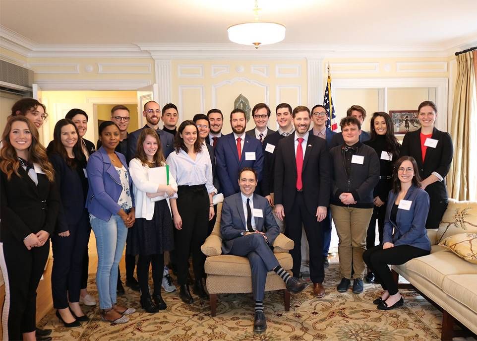 Les étudiantes et les étudiants ayant participé à la simulation de la crise des missiles de Cuba prennent la pose dans un salon du Consulat général des États-Unis à Québec en compagnie du consul général adjoint Michael Agner, à l'avant et debout à côté du professeur Jonathan Paquin, assis dans un fauteuil.