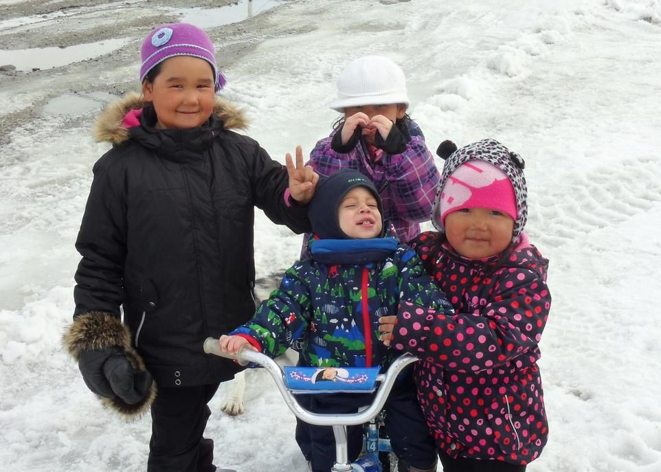 Des enfants inuit s'amusent avec un petit garçon non inuit sur son vélo dans le village d'Inukjuak.