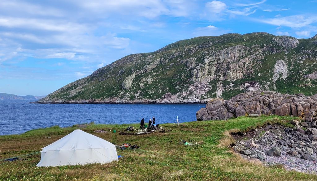 <p>L’aire de fouilles des archéologues à l’anse à Henry, avec l’île du Grand Colombier au loin. On aperçoit une tente blanche à proximité qui servait d’abri et où était entreposé l’équipement.</p>