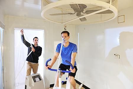 Cette chambre hypoxique, qui vient d'être construite au Département de kinésiologie, permet de recréer l'atmosphère pauvre en oxygène qu'on trouve en altitude. Elle sera utilisée par François Billaut, en arrière-plan, pour ses projets de recherche portant sur les effets physiologiques de l'exposition à l'hypoxie. Des athlètes d'élite de la région de Québec y auront aussi recours pour leur entraînement. Mathieu Lanoue, un membre de l'équipe du professeur Billaut, démontre l'un des usages possibles de cet équipement.