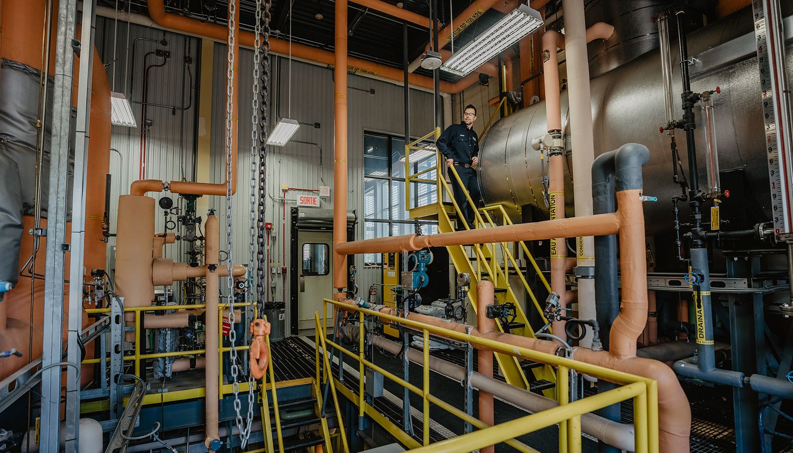 Pour chauffer ses bâtiments, l'Université Laval utilise un système à la vapeur d'eau. Elle produit cette vapeur grâce à deux centrales d'énergie. Elles sont gérées 24 heures par jour et 7 jours par semaine par des mécaniciennes et mécaniciens de machines fixes qui surveillent et entretiennent le système, les équipements et les infrastructures souterraines. Sur la photo, on aperçoit le mécanicien de machines fixes Maxime Gauthier à l'intérieur de la centrale d'énergie principale.