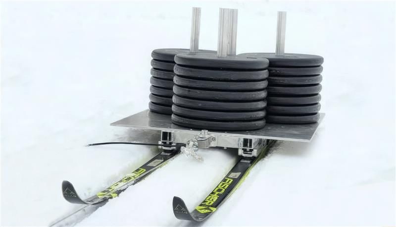 Le système conçu par les chercheurs comprend un chariot monté sur des skis sur lequel est installée une charge simulant un skieur. Le chariot est relié à un treuil et les chercheurs mesurent la force requise pour mettre le chariot en mouvement et pour le faire avancer à une vitesse donnée.