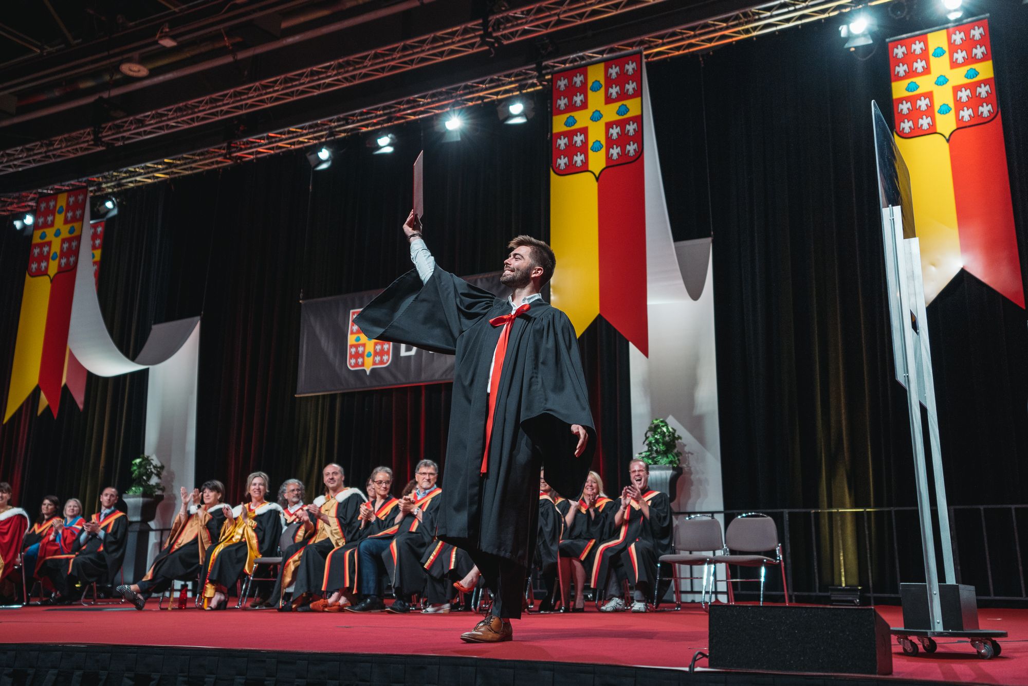 <p>Diplômé montrant fièrement son diplôme sur scène à la cérémonie de collation des grades</p>