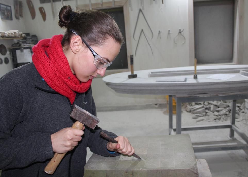 L'étudiante Evelyne Vincent en train de tailler un bloc de calcaire à l'atelier du tailleur de pierre Adrien Bobin.