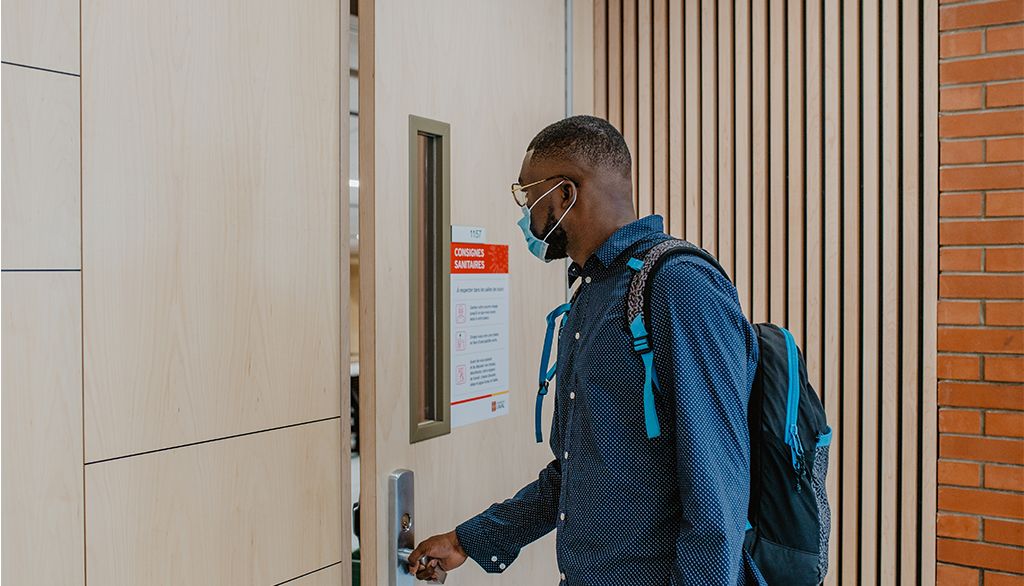 <p>Un étudiant portant un masque chirurgical entre dans une salle de classe à L'Université aval.</p>