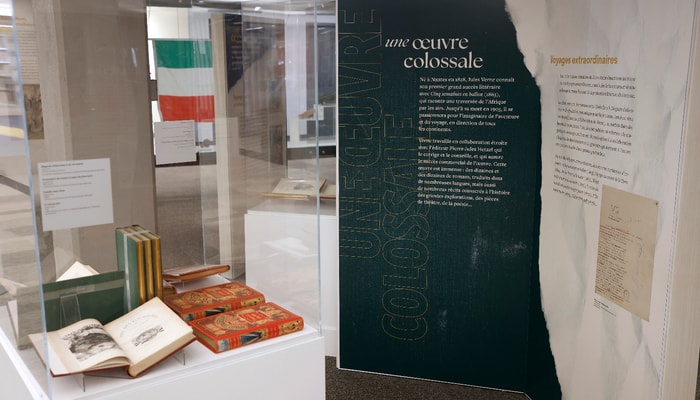 Cette section de l'exposition traite de l'importance de l'œuvre de Jules Verne. Celle-ci comprend, entre autres, une soixantaine de romans traduits dans de nombreuses langues. Le premier grand succès littéraire de l'écrivain fut Cinq semaines en ballon, publié en 1863. Plus loin, on aperçoit le drapeau tricolore des Patriotes dans la section consacrée à Famille-Sans-Nom.