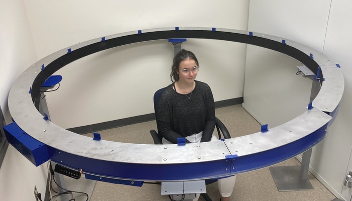 Anne-Sophie Côté, étudiante en sciences de la réadaptation et membre de l'équipe du professeur Philippe Fournier, au centre d'une structure dans laquelle sont intégrés 8 haut-parleurs disposés sur 360 degrés. Ce système, conçu par le professeur François Bergeron, diffuse des ambiances sonores de la vie quotidienne qui permettent de mesurer le seuil de dérangement et le seuil d'inconfort.