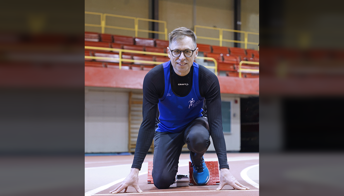 Le professeur Jérôme Frenette en vêtements de course à pied, en position dans un bloc de départ sur la piste de 200 mètres du PEPS, au mois de mars 2025