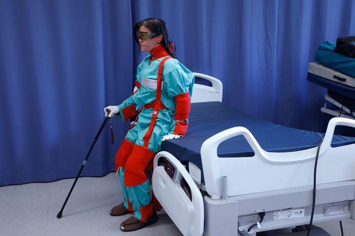 La combinaison de vieillissement (geri suit) vise à restreindre les mouvements, tout en les rendant plus exigeants physiquement. Vêtue d'une telle combinaison, la technicienne spécialisée en simulation Vanessa Massicotte s'assoit de manière pénible sur le lit d'hôpital.