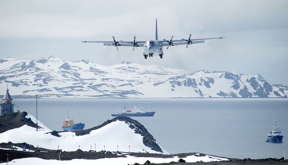 <p>Un avion de transport C-130 Hercules en approche pour atterrir à l’aérodrome du Teniente Rodolfo Marsh Martin, avec des navires à la gare maritime de Fildes Bay en arrière-plan, et l’église russe à gauche. Administré par le Chili, cet aérodrome situé sur l'Île du Roi-George est le plus au nord du continent antarctique. Il est au cœur du projet de recherche codirigé par le professeur Dermot Antoniades.</p>