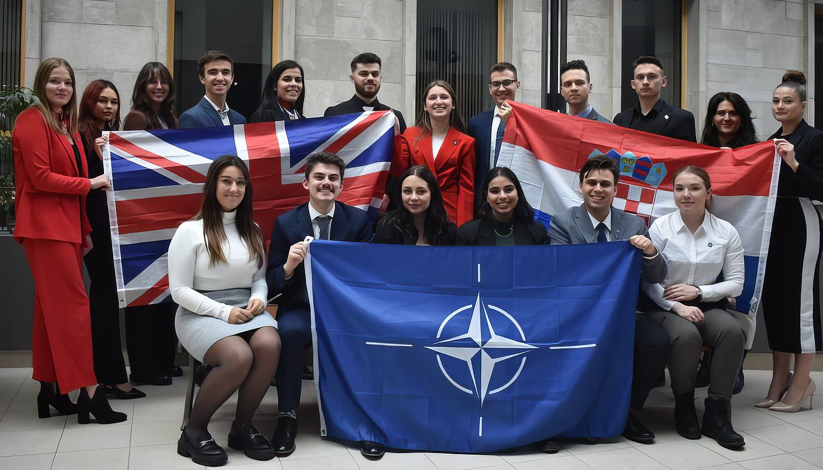 <p>Les 18 membres de la délégation de l’Université Laval avant leur départ pour Washington. On reconnaît le drapeau de l’OTAN à l’avant et les drapeaux britannique et croate à l’arrière.</p>