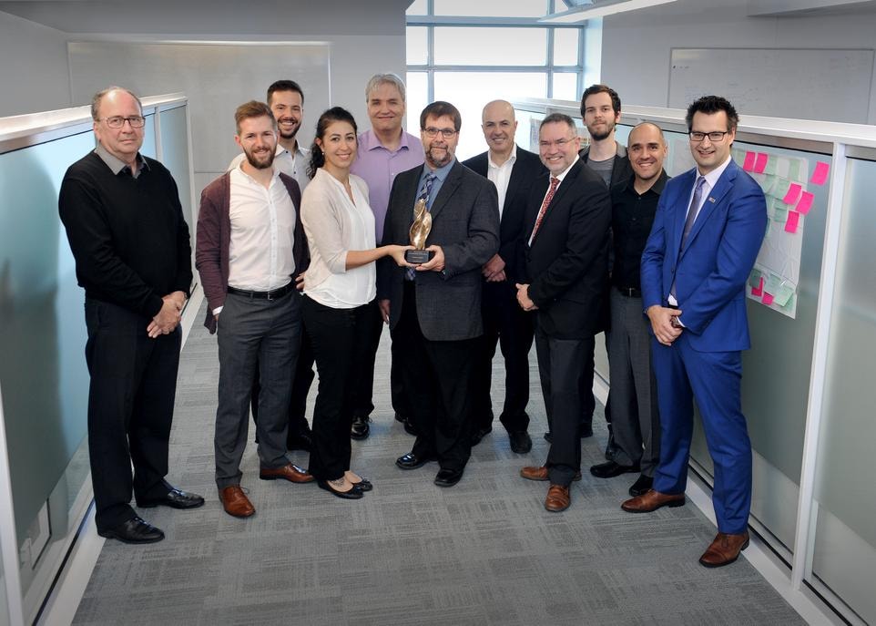 Une grande partie de l'équipe de la DTI ayant réalisé le projet Méthodologie. On reconnaît, tenant le Prix d'excellence, la chargée de projet Pauline Robert et le directeur de la DTI, Michel Thibault. Le vice-recteur adjoint aux systèmes d'information, René Lacroix, et le vice-recteur exécutif et au développement, Éric Bauce, se trouvent respectivement à droite et derrière le directeur de la TDI. Enfin, le directeur de la gestion du portefeuille et du développement des ressources informationnelles à la DTI, Dave Fiset, est à droite sur la photo.