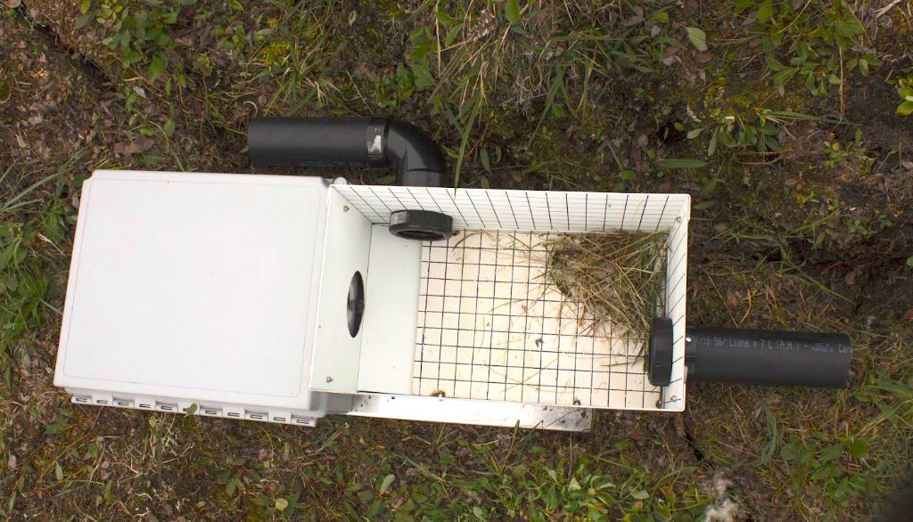 <p>Vue en plongée du dispositif de monitorage des lemmings. La boîte de gauche contient les composantes électroniques, la batterie et la caméra infrarouge. Le couvercle de la boîte de droite a été retiré pour exposer l'enceinte dans laquelle circulent les lemmings. Les deux courts tuyaux qui donnent accès à l'enceinte sont intégrés, par les lemmings eux-mêmes, à leur réseau de tunnels.</p>