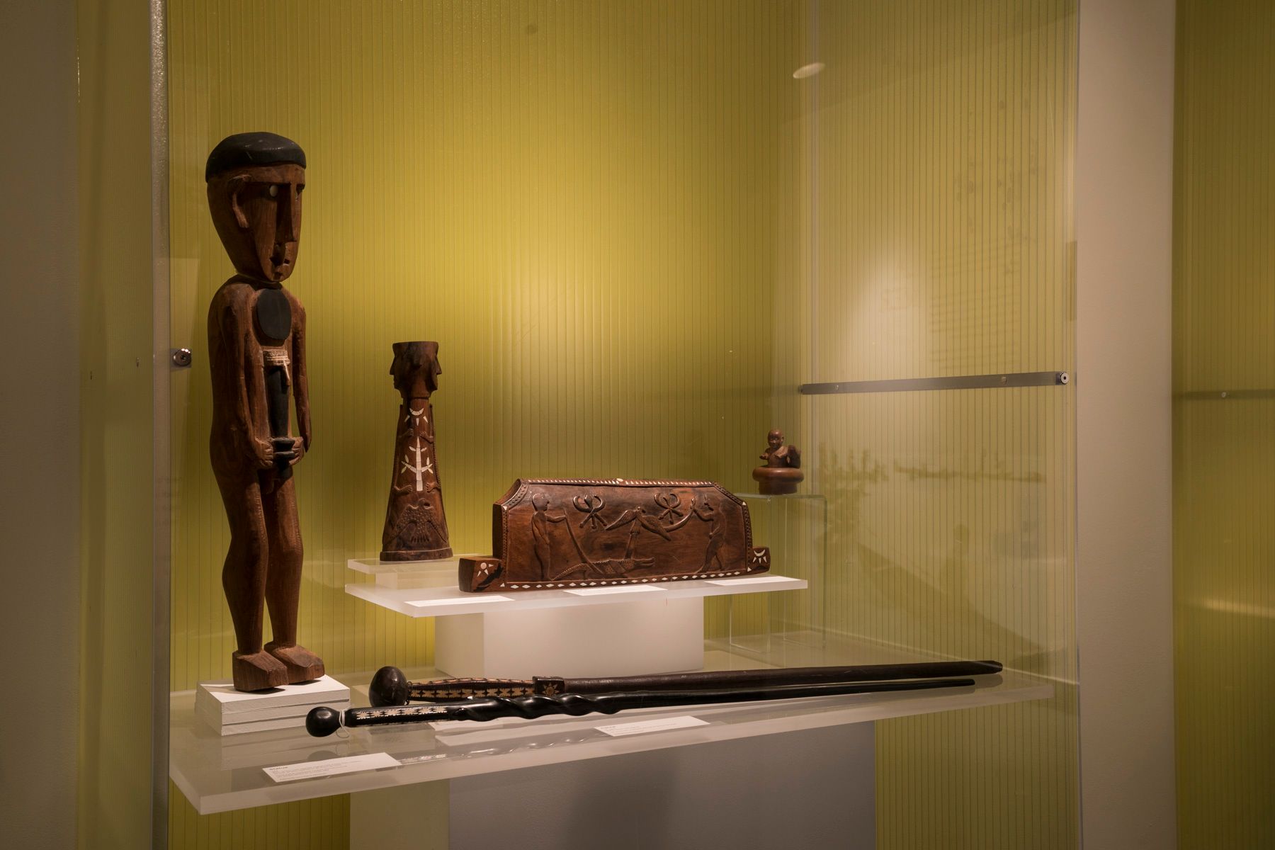 <p>Des vitrines mettent en valeur de nombreux artéfacts. Parmi eux, mentionnons cette sculpture de bois représentant le premier homme lau tenant devant lui une arme appelée casse-tête. Cette sculpture a été confectionnée expressément pour Pierre Maranda en 1967. À côté se trouve un magnifique bas-relief mettant en scène une synthèse des symboles importants de la culture lau, notamment l’oiseau, le crocodile, la massue et le casse-tête.</p>