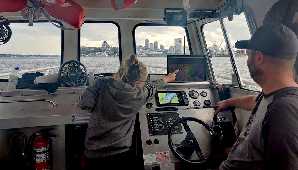 Dans le poste de pilotage du Louis-Edmond-Hamelin avec vue sur Québec. Le capitaine de l’embarcation, Benoit Cotton, est à droite et l’hydrographe, Natalie Pisciotto, est à gauche. Elle pointe sur l’écran les acquisitions qui sont faites en temps réel par le sondeur multifaisceaux.