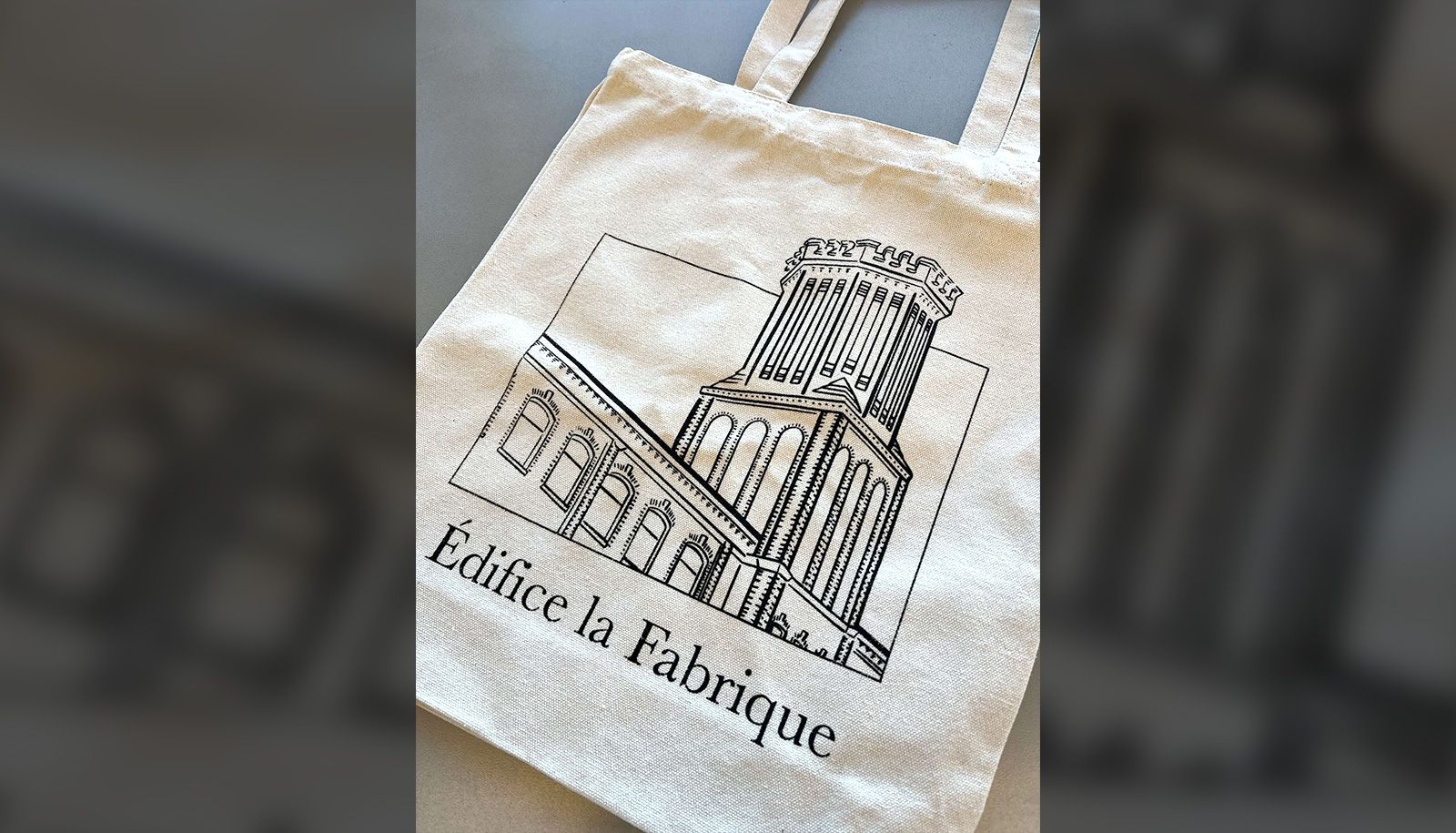 De plus en plus essentiel dans notre société pour un grand nombre de consommatrices et consommateurs, le sac réutilisable permet de réduire son empreinte écologique. Cet objet du quotidien est aussi un accessoire de mode. Ce sac de coton naturel, réalisé par Léa Guimond et Frédérique Leblond, toutes deux inscrites au baccalauréat en design graphique, a été conçu à l'image de l'édifice La Fabrique ou de l'identité visuelle du marché Volumique. Il a été imprimé en sérigraphie.