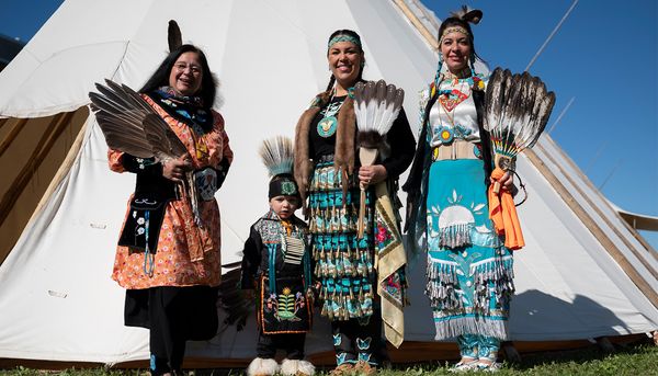 Le 30 septembre 2022, la Journée nationale de la vérité et de la réconciliation, tenue dans le Grand Axe, avait mis en vedette le petit Liam Michaud, un jeune danseur ojibwé wendat de Wendake. L’enfant reviendra cette année. Sur la photo, il est accompagné de sa mère, Vicky Giguère, ojibwée, deuxième à droite. Les deux autres femmes, Julie Gros-Louis et Aroussen Gros-Louis, sont également des résidentes de Wendake. Tous les quatre posent devant un shaputuan érigé pour l’occasion. Cette grande tente traditionnelle sert de maison de transmission de la culture chez les Innus.